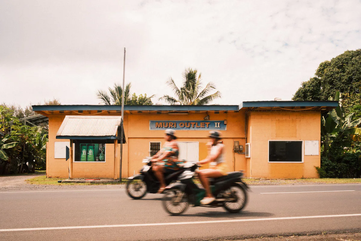 Scooters passing local building in Rarotonga, sunny afternoon